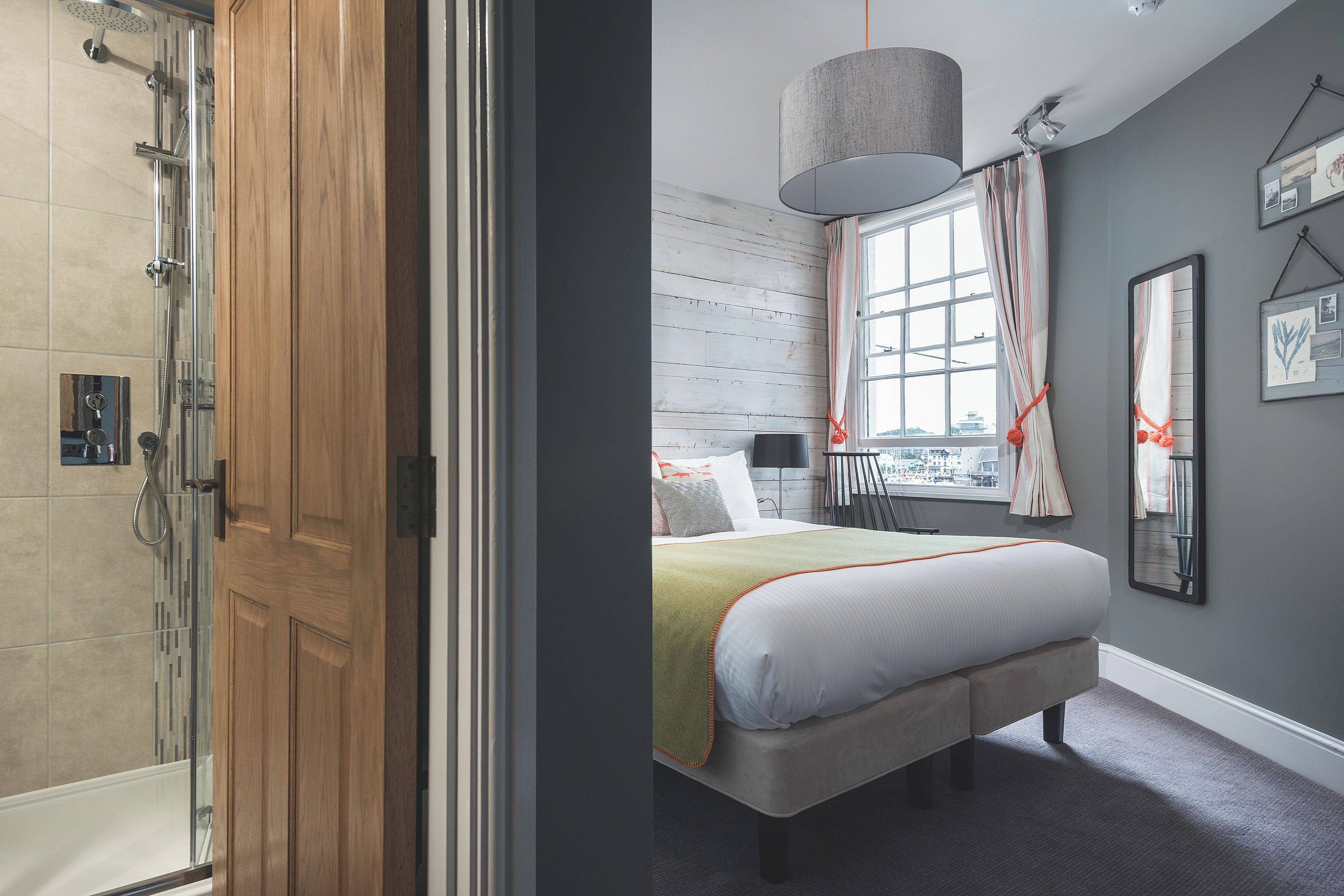 A hotel room with a large bed, a window with curtains, a hanging lamp, and a view of the city.