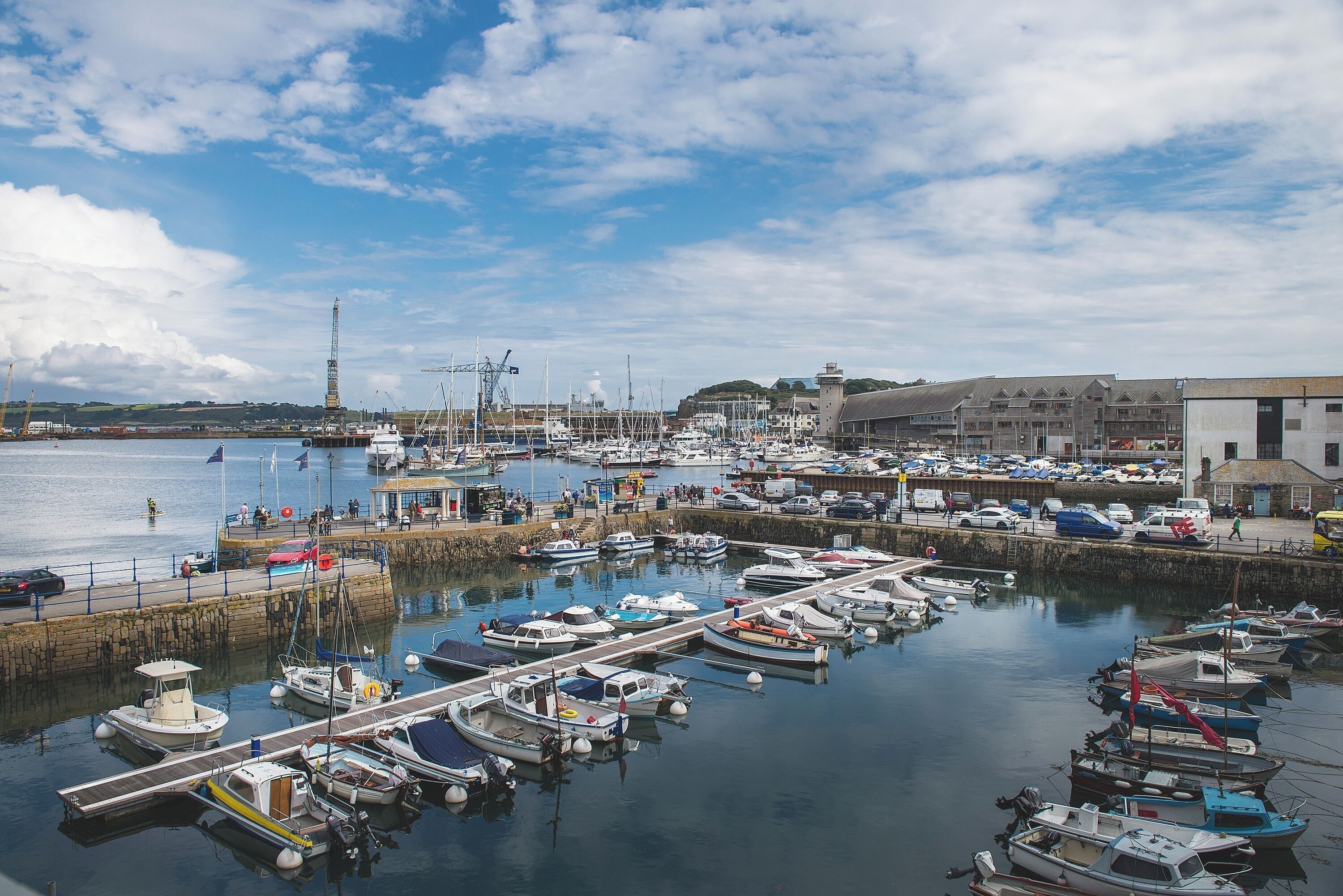 A marina with boats docked, a pier, and buildings in the background.