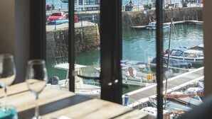 A view from a window overlooking a marina with boats docked, a wooden table with a glass of blue liquid, and a napkin. - Chainlocker (Falmouth)