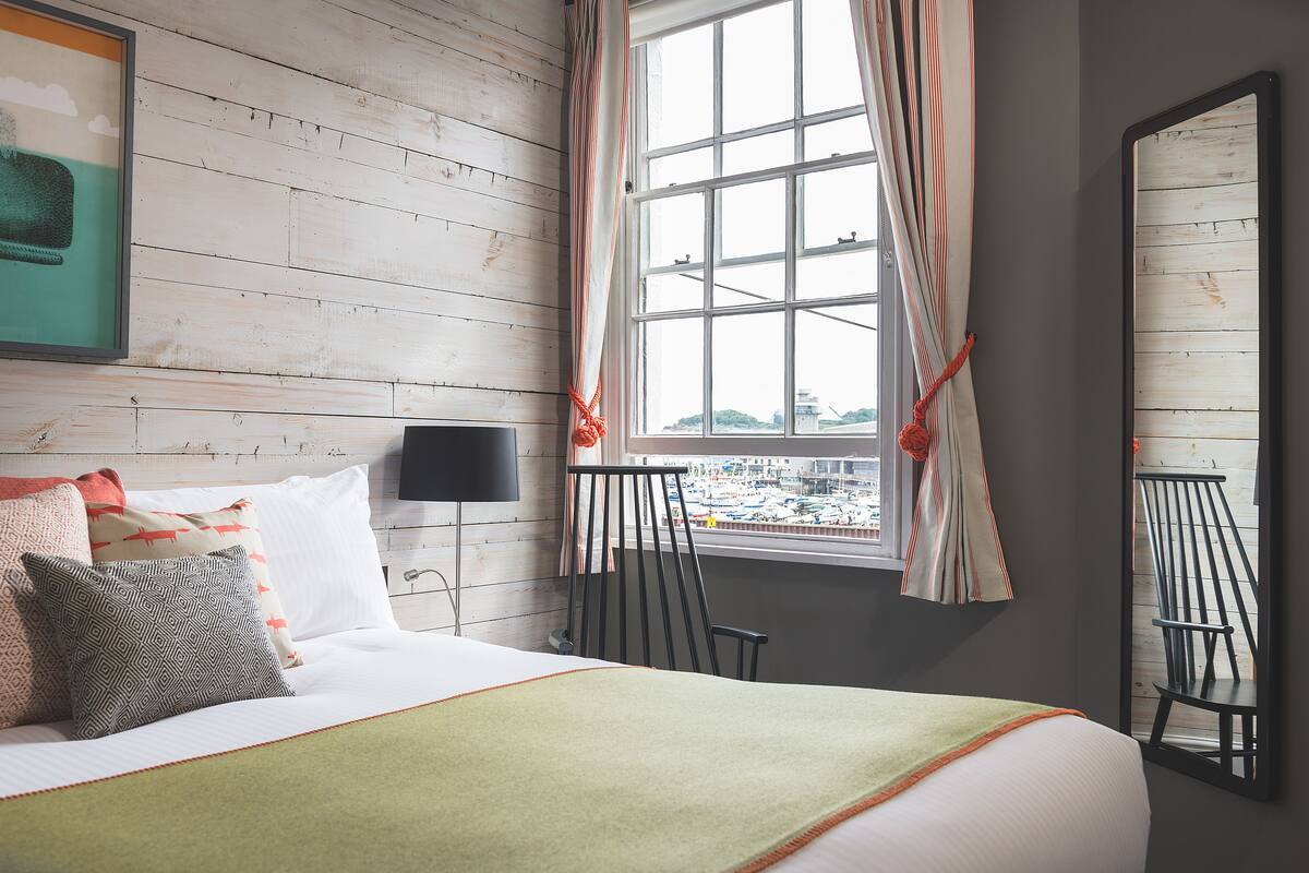 Ein Hotelzimmer mit Bett, einem Vorhangfenster, einem Sessel und einem an der Wand befestigten Fernseher.