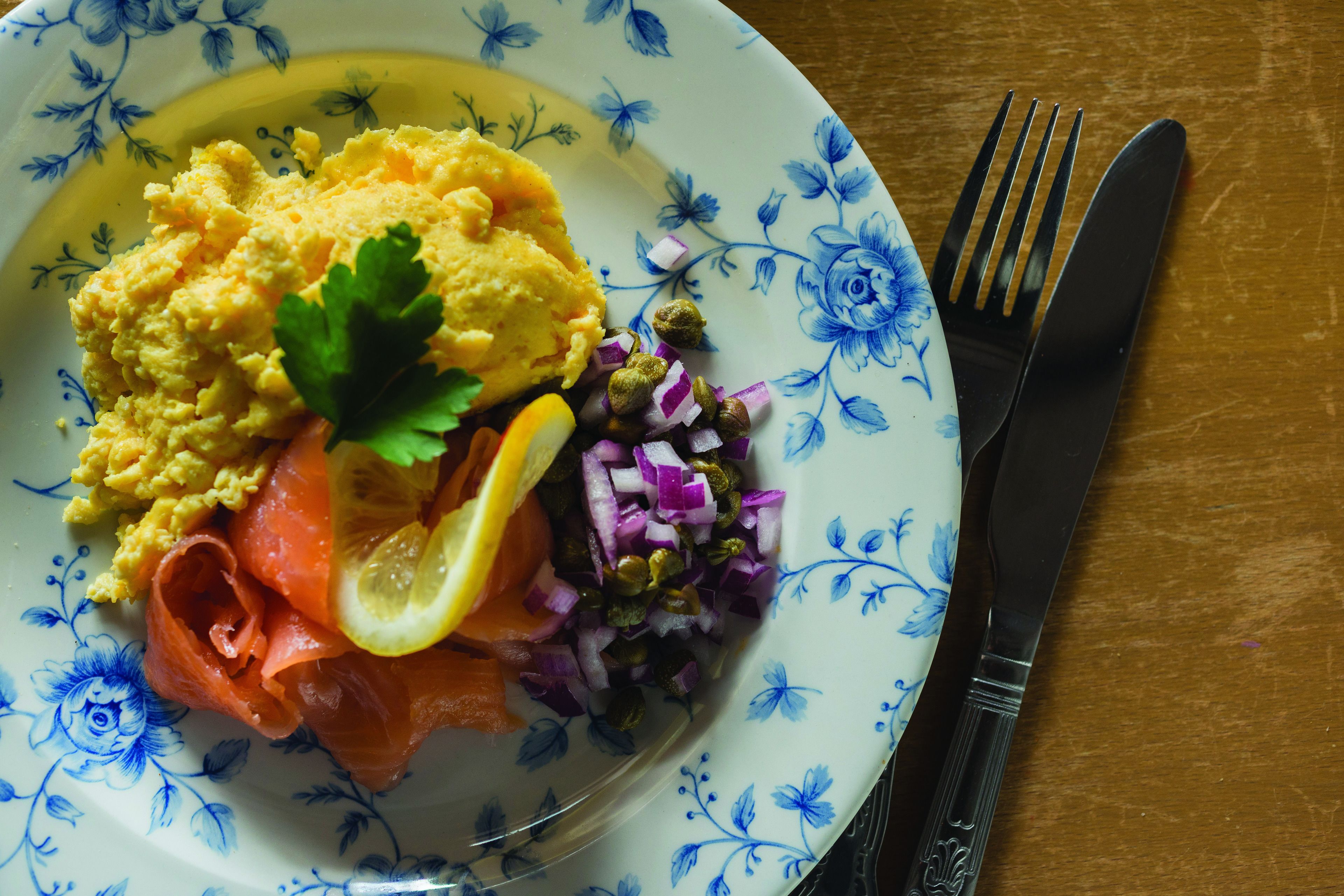 A plate with scrambled eggs, smoked salmon, red onion, capers, and a lemon wedge, garnished with parsley.