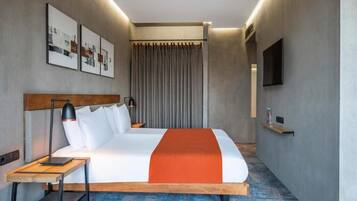 A modern hotel room with a large bed, a bedside table, a lamp, a TV, and a curtain.