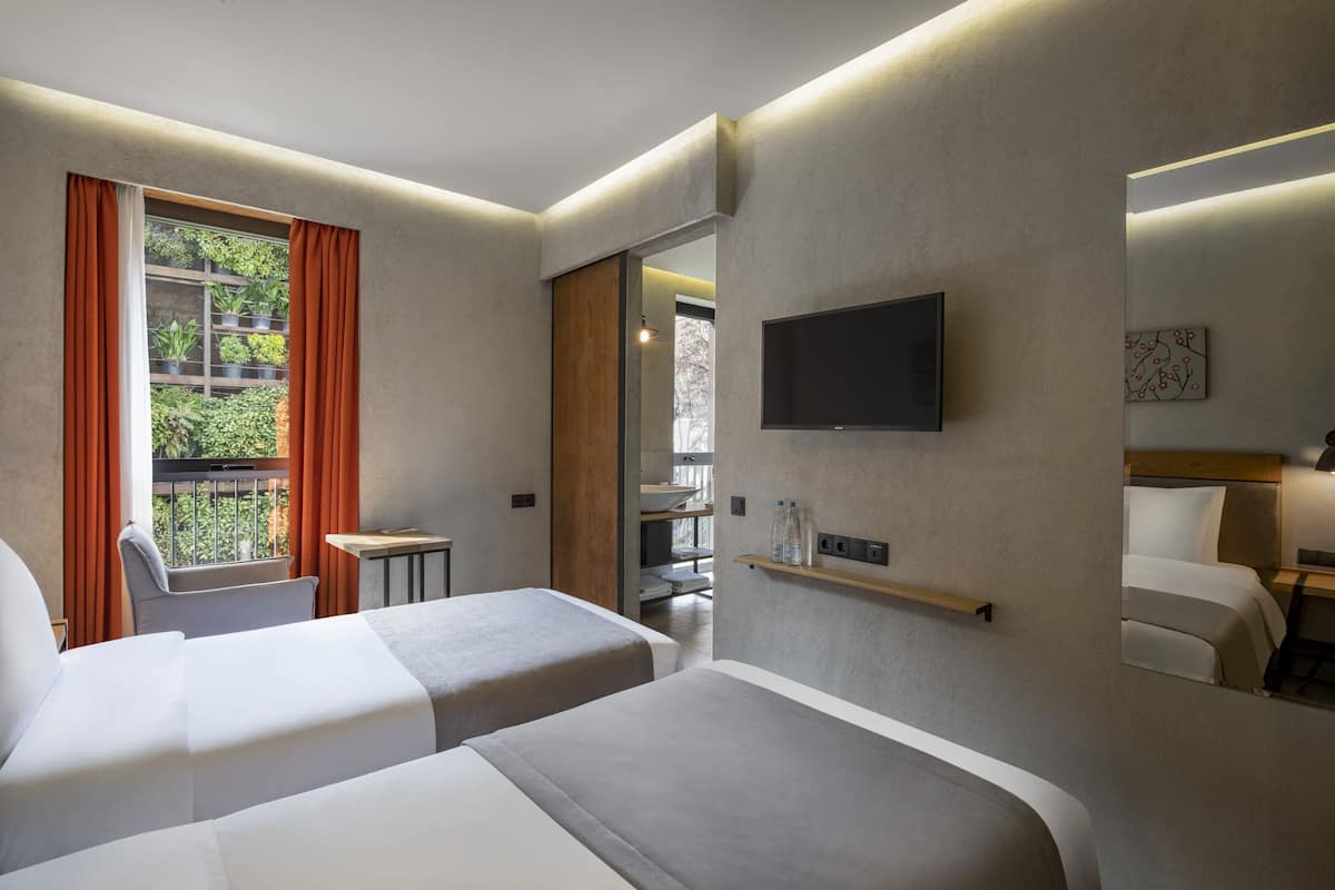 A hotel room with two beds, a TV, a small table, and a window with curtains.