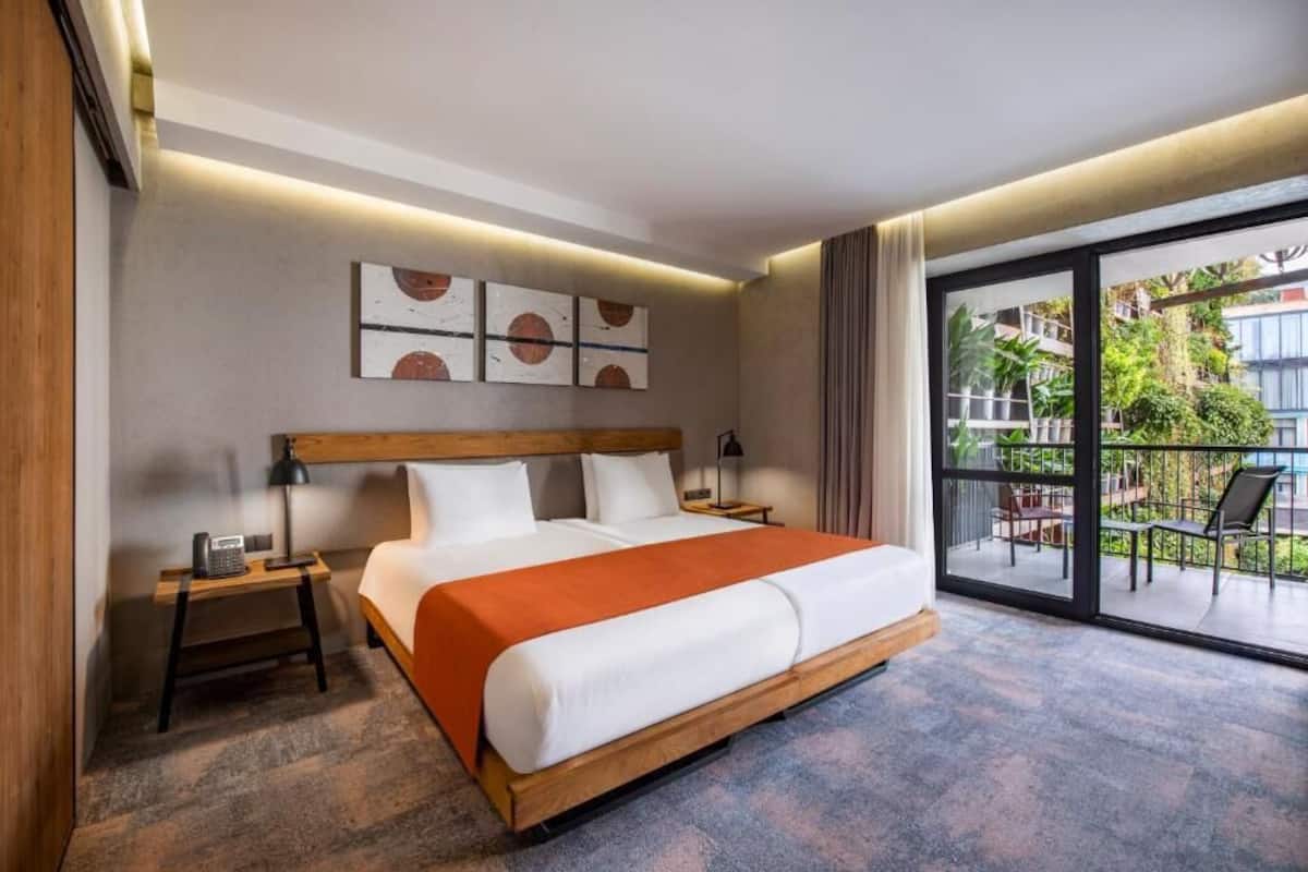 A hotel room with a large bed, a nightstand, a lamp, and a view of the outdoor balcony.