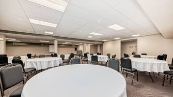 Un salón de conferencias con mesas redondas, sillas y un techo alto con iluminación empotrada.