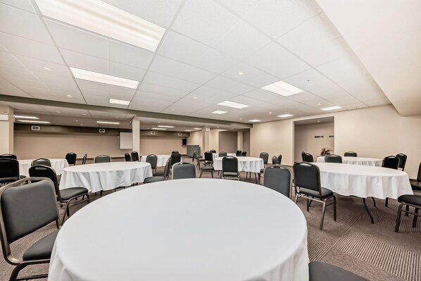 Un salón de conferencias con mesas redondas, sillas y un techo alto con iluminación empotrada.