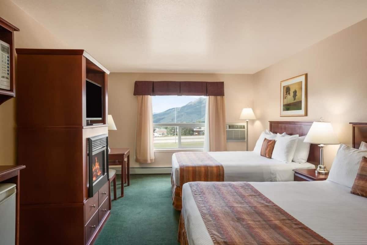 Ein Hotelzimmer mit zwei Betten, einem Kamin, einem Schreibtisch und einem Fenster mit Blick auf die Berge.