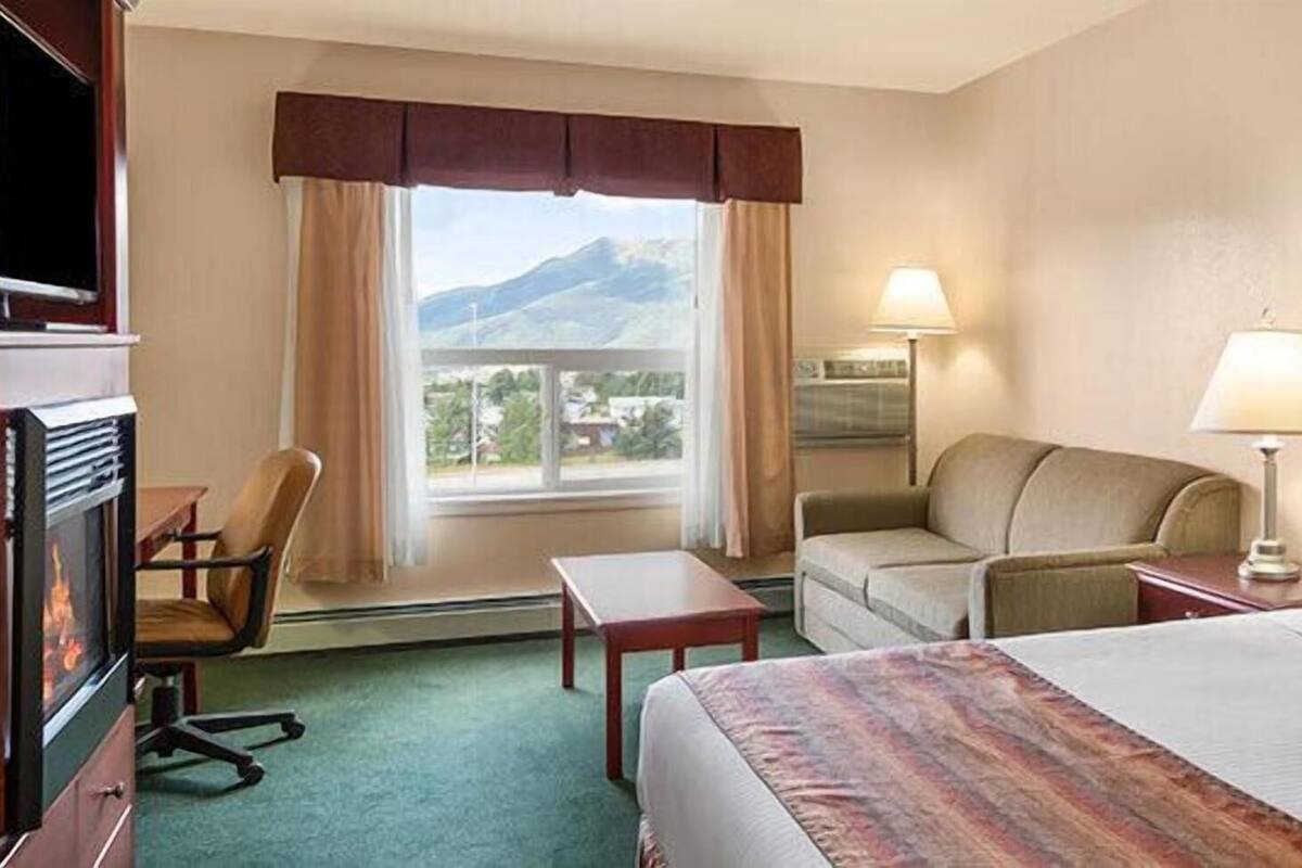 Ein Hotelzimmer mit Bett, Schreibtisch, Sessel, Sofa, Fernseher und Fenster mit Bergblick.