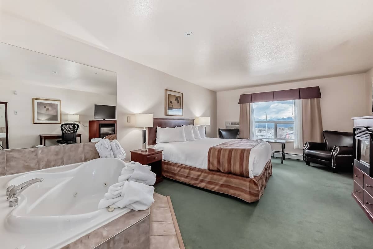 Ein Hotelzimmer mit einer großen Badewanne, einem Bett mit gestreifter Bettwäsche, einem Schreibtisch mit Lampe, einem Fernseher und Blick auf die Stadt durch das Fenster.