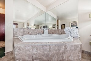 A modern bathroom with a large freestanding bathtub, a large mirror, and marble tiles.