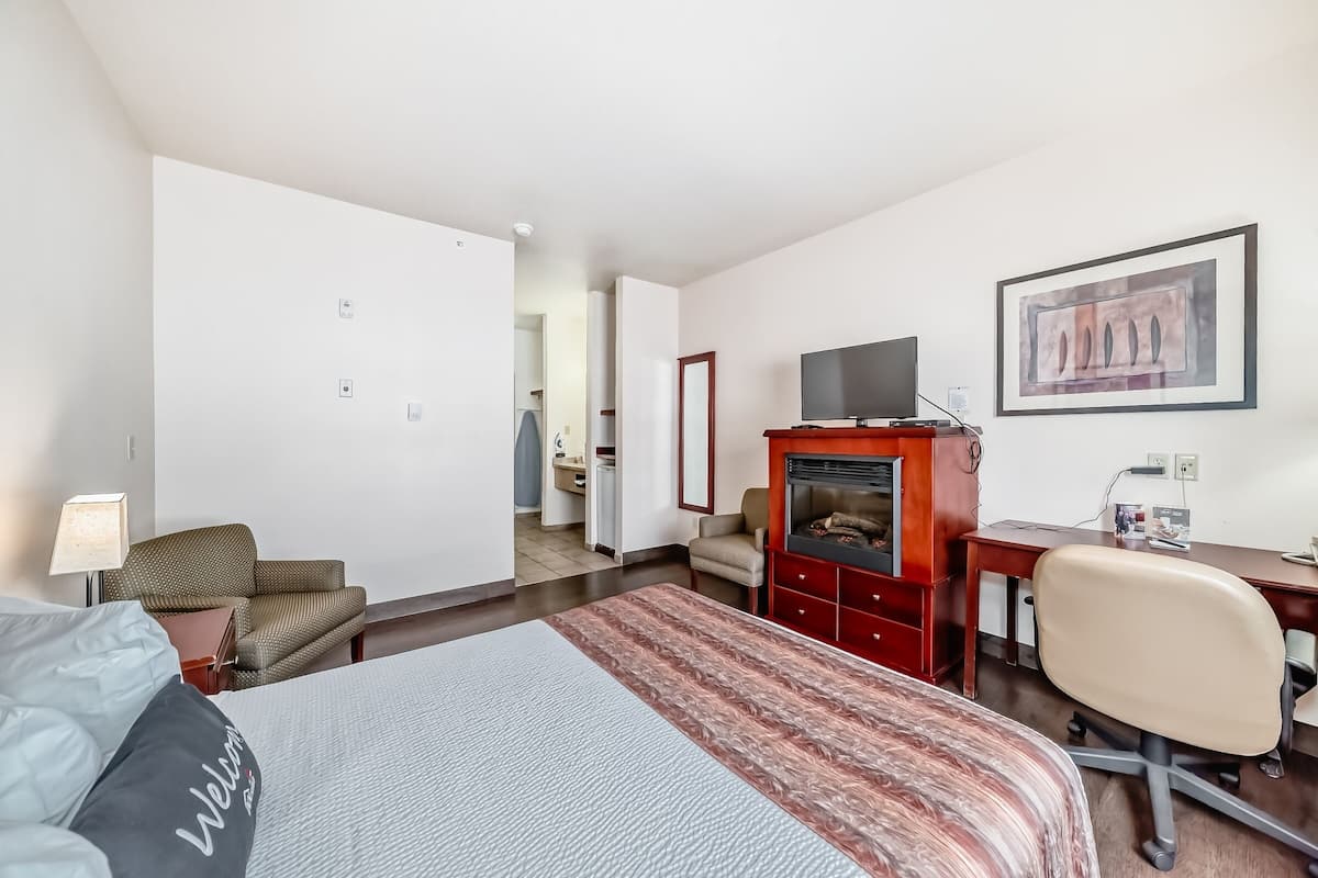 Ein Hotelzimmer mit Bett, Schreibtisch, Fernseher, Stuhl und einem Gemälde an der Wand.
