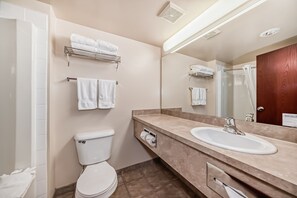 A modern bathroom with a toilet, sink, and shower. There are multiple towels on the wall and a mirror above the sink.