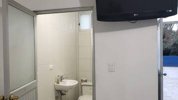 Un baño con inodoro, lavamanos y televisor montado.