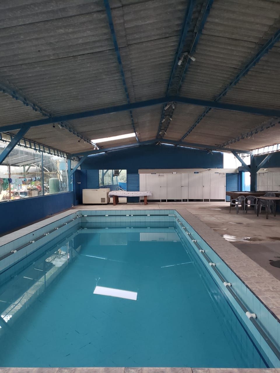 Una piscina interior con suelo de baldosas, un banco y taquillas al fondo.