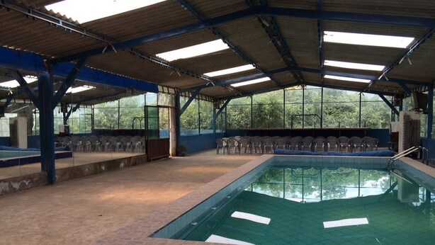 An indoor swimming pool with a tiled floor, a pool with a blue border, and a roof supported by blue beams. - Hostal Davinci Mitad del Mundo (San Antonio de Pichincha)