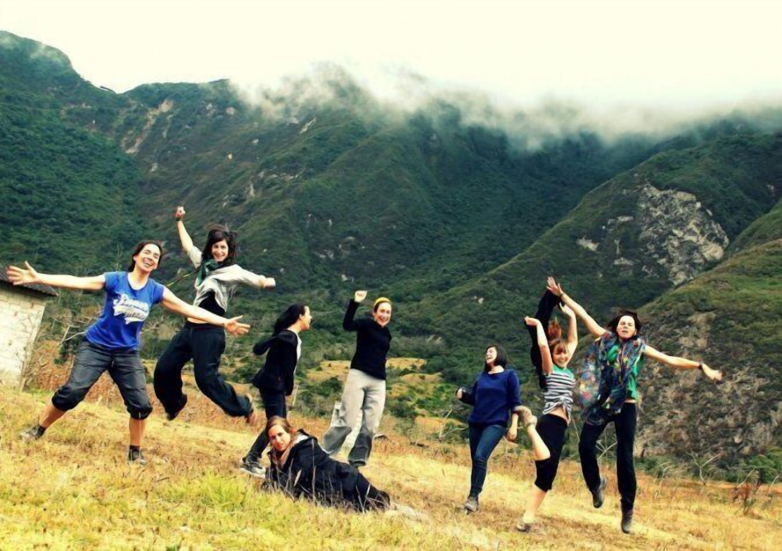 A group of people jumping on a grassy hillside with a mountainous backdrop.