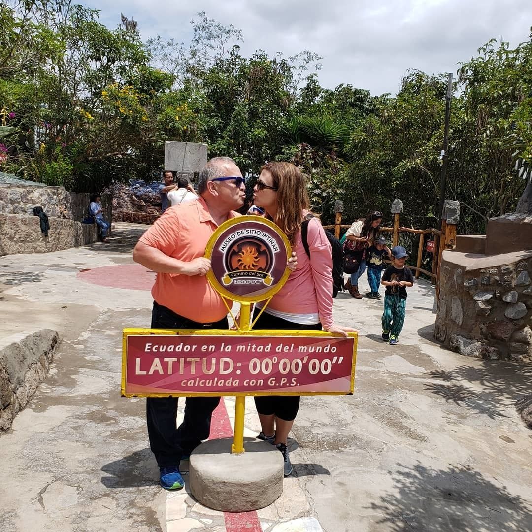 A sign with a circular emblem and text indicating a location in Ecuador, with a stone base and a yellow pole.