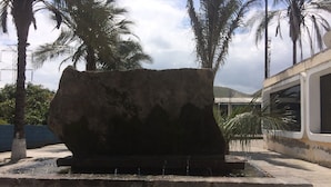 A large rock sculpture in an outdoor setting with palm trees and a building in the background. - Hostal Davinci Mitad del Mundo (San Antonio de Pichincha)