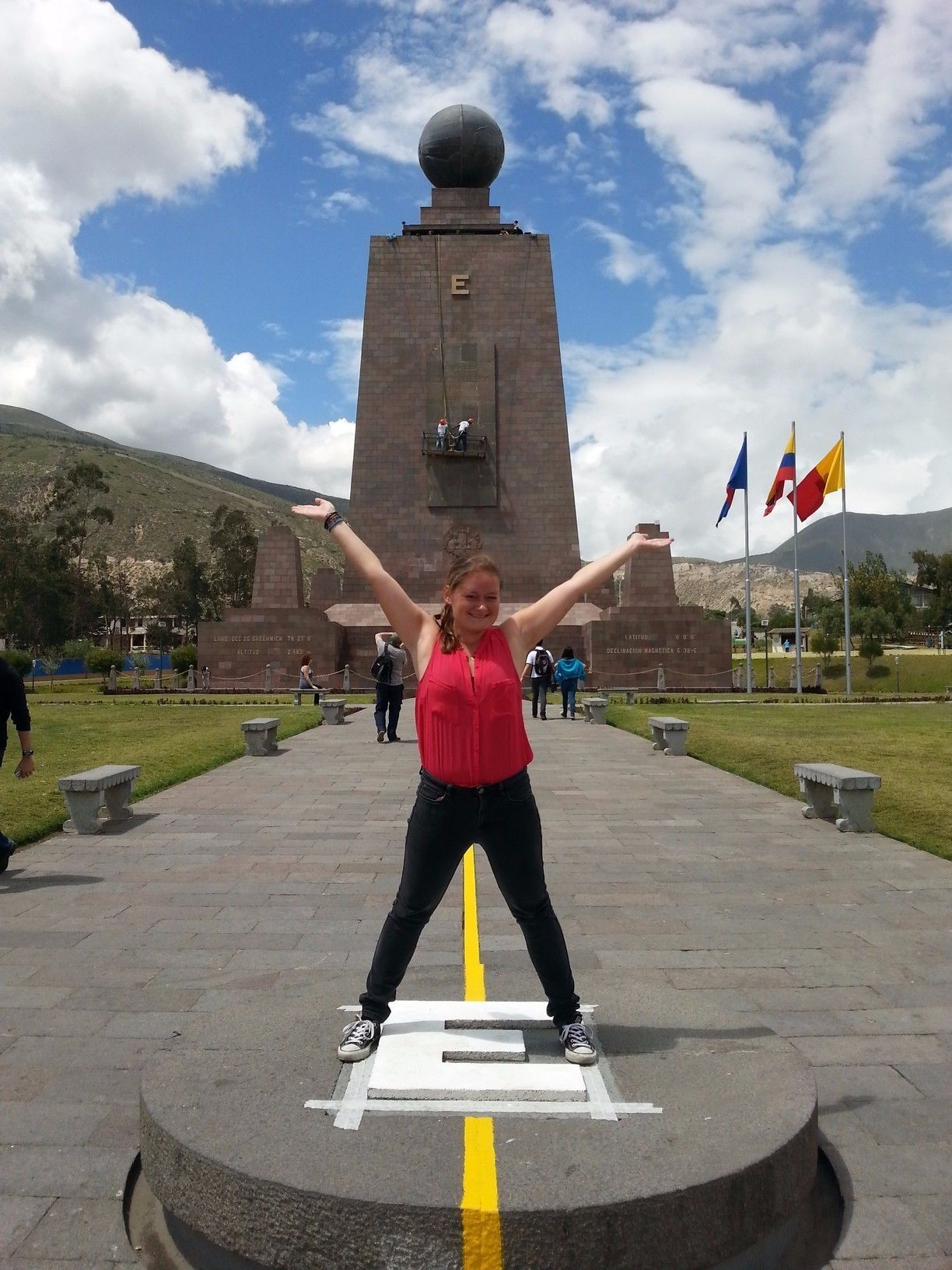 A monument with a spherical top and a letter 'E' on its base, surrounded by flags and people.
