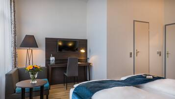 A hotel room with a bed, a desk with a chair, a TV, and a lamp.