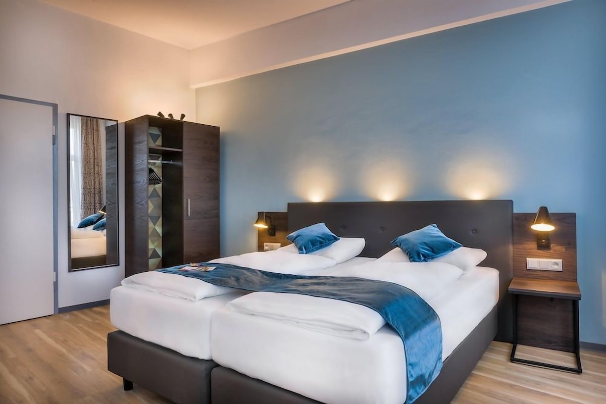 Un lit double avec une tête de lit, des lampes de chevet et un plaid bleu.