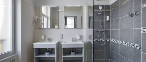 A modern bathroom with two sinks, a shower, and a glass partition.