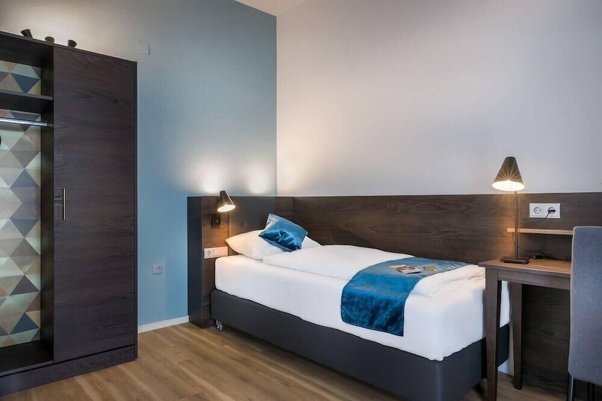 A bedroom with a bed, bedside lamps, a desk, and a wardrobe.