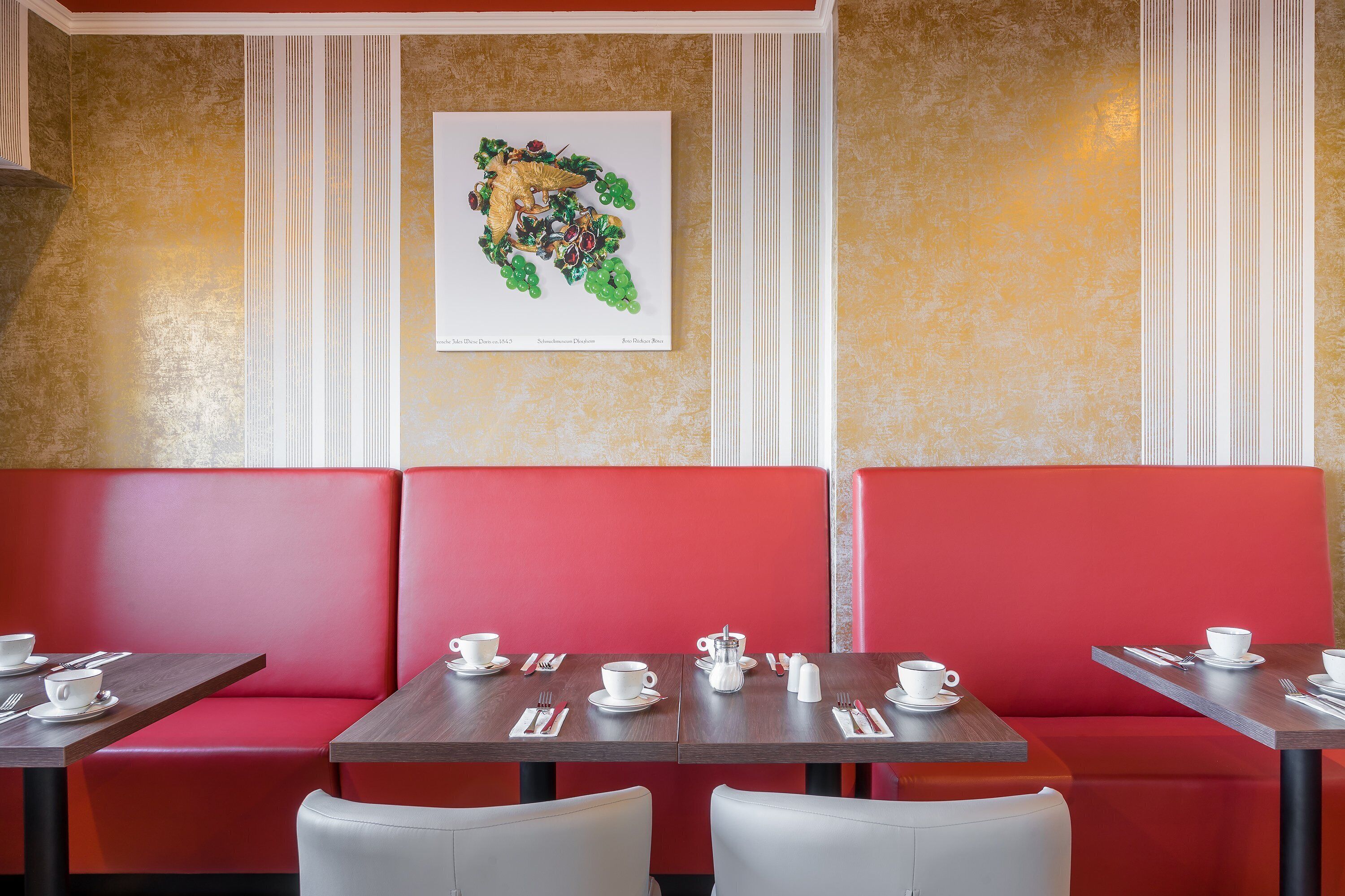 A restaurant with red booths and tables, each set with white cups, saucers, and cutlery.