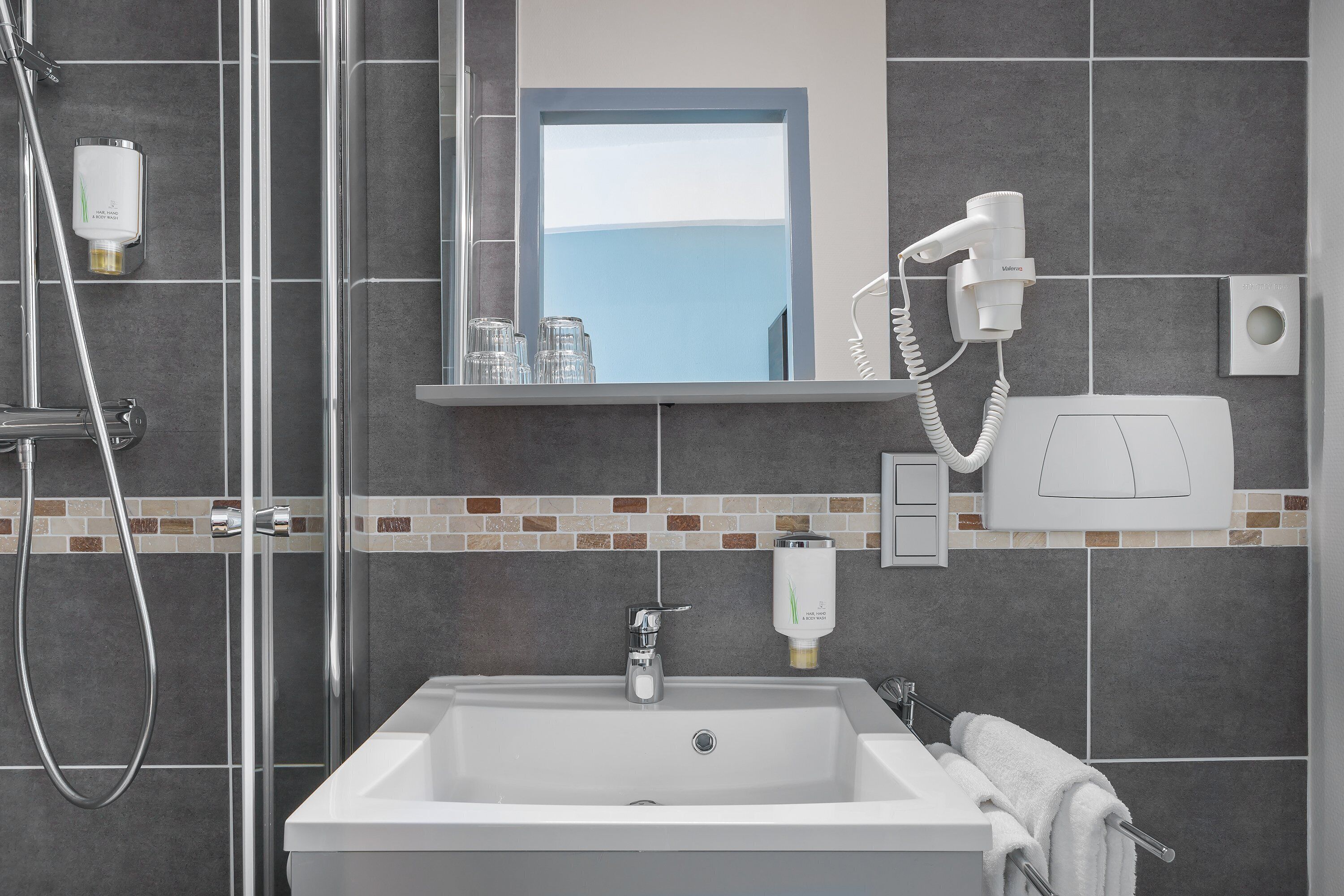 A modern bathroom with a shower, a sink, a mirror, and a hairdryer.