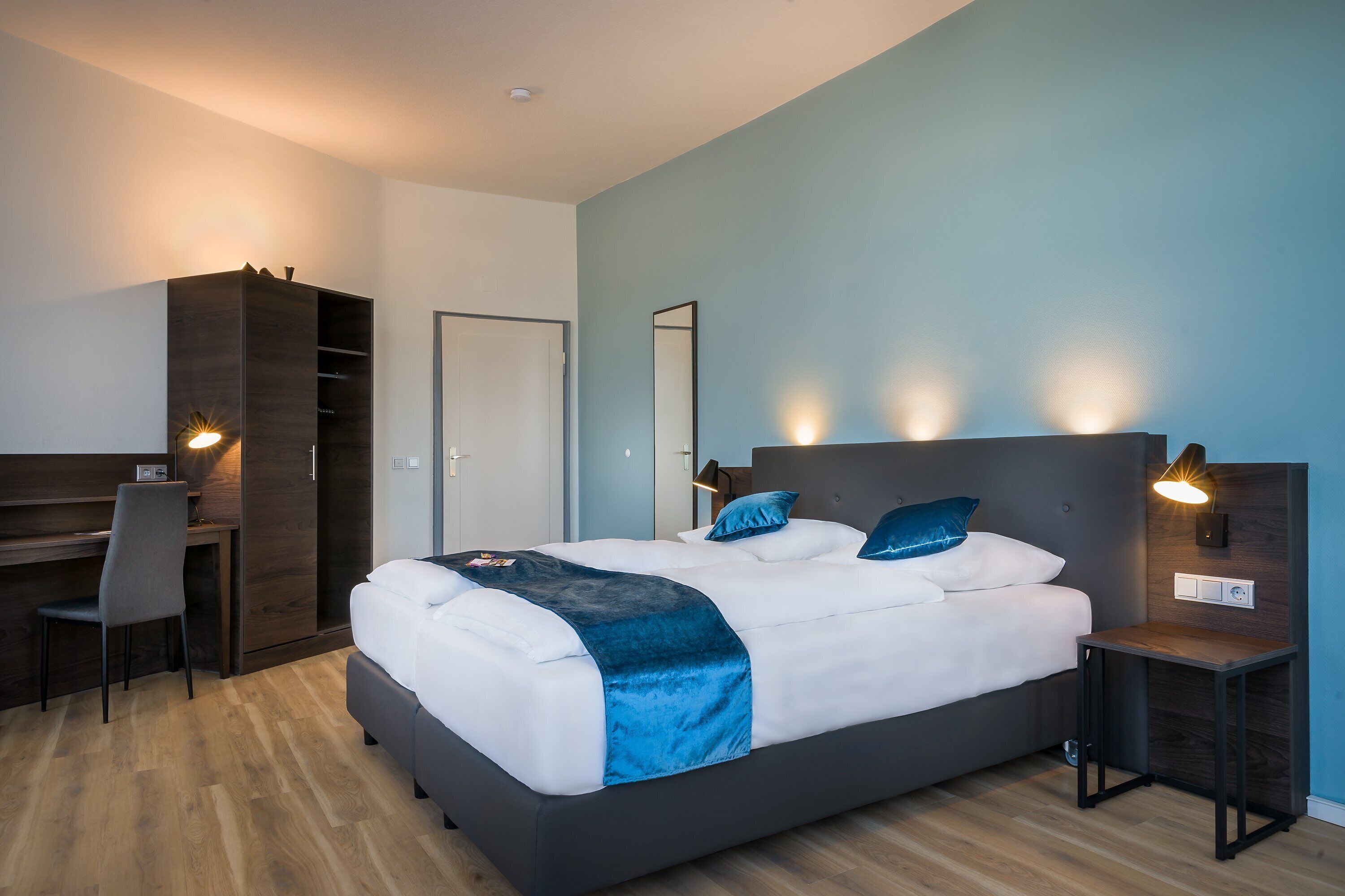 Une chambre moderne comprenant un lit, un bureau et une chaise, une armoire et une table de chevet avec une lampe.