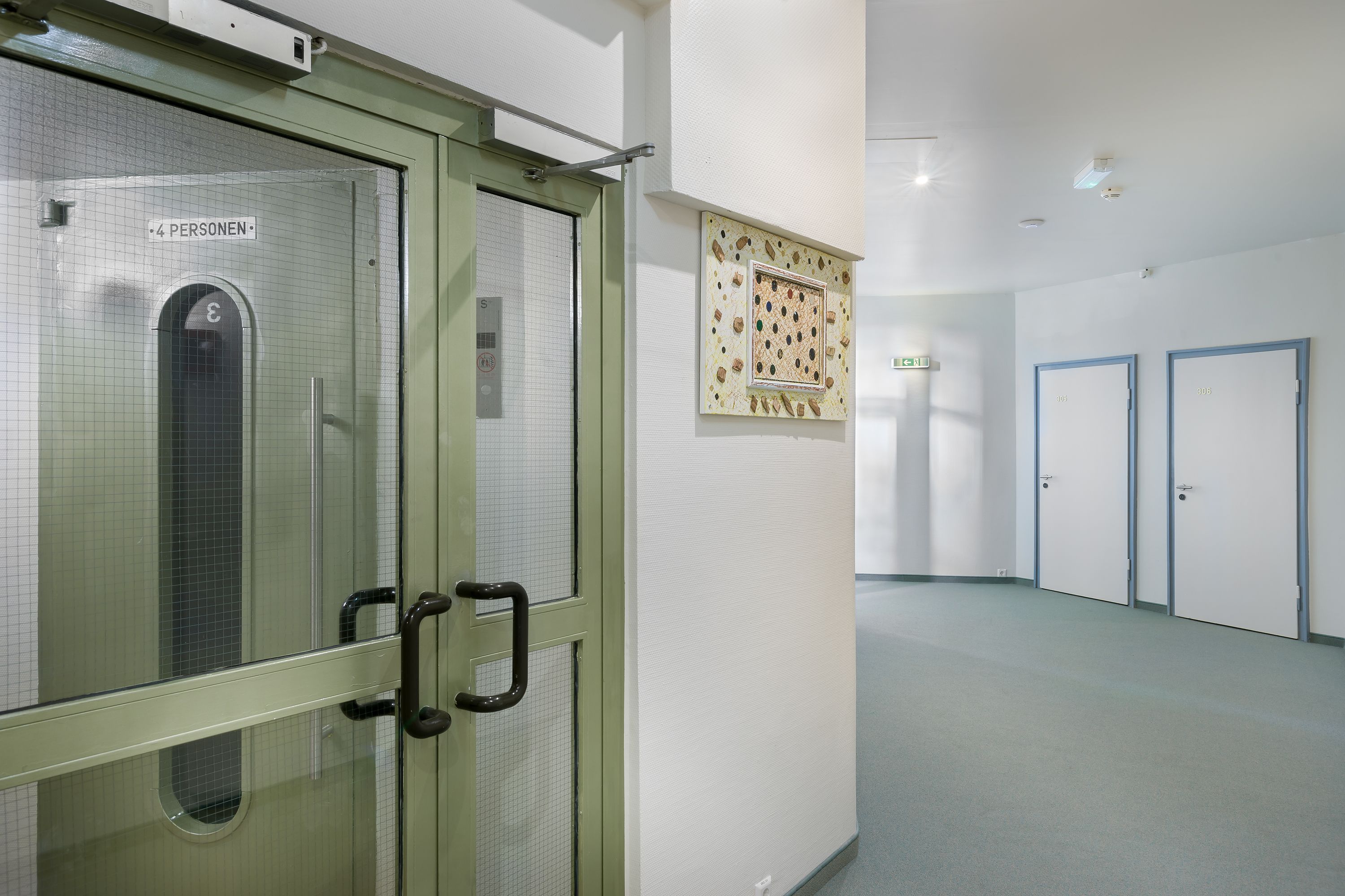 A hallway with a glass door marked "4 Personen" and a framed artwork on the wall.