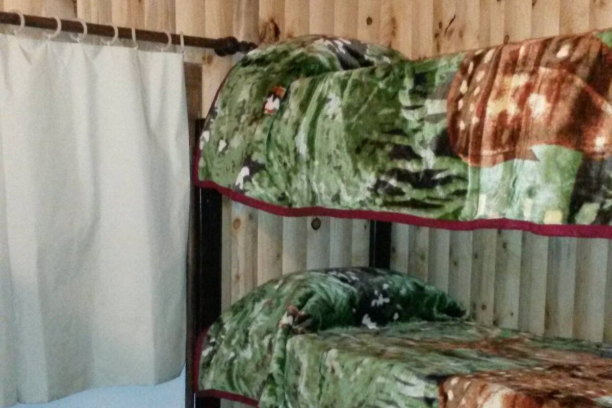 Een stapelbed met camouflage beddengoed in een kamer met houten wanden en een witte kast.