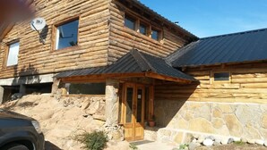 A log cabin with a stone foundation, a wooden door, and a satellite dish. - Hostel Andino (Villa Pehuenia)