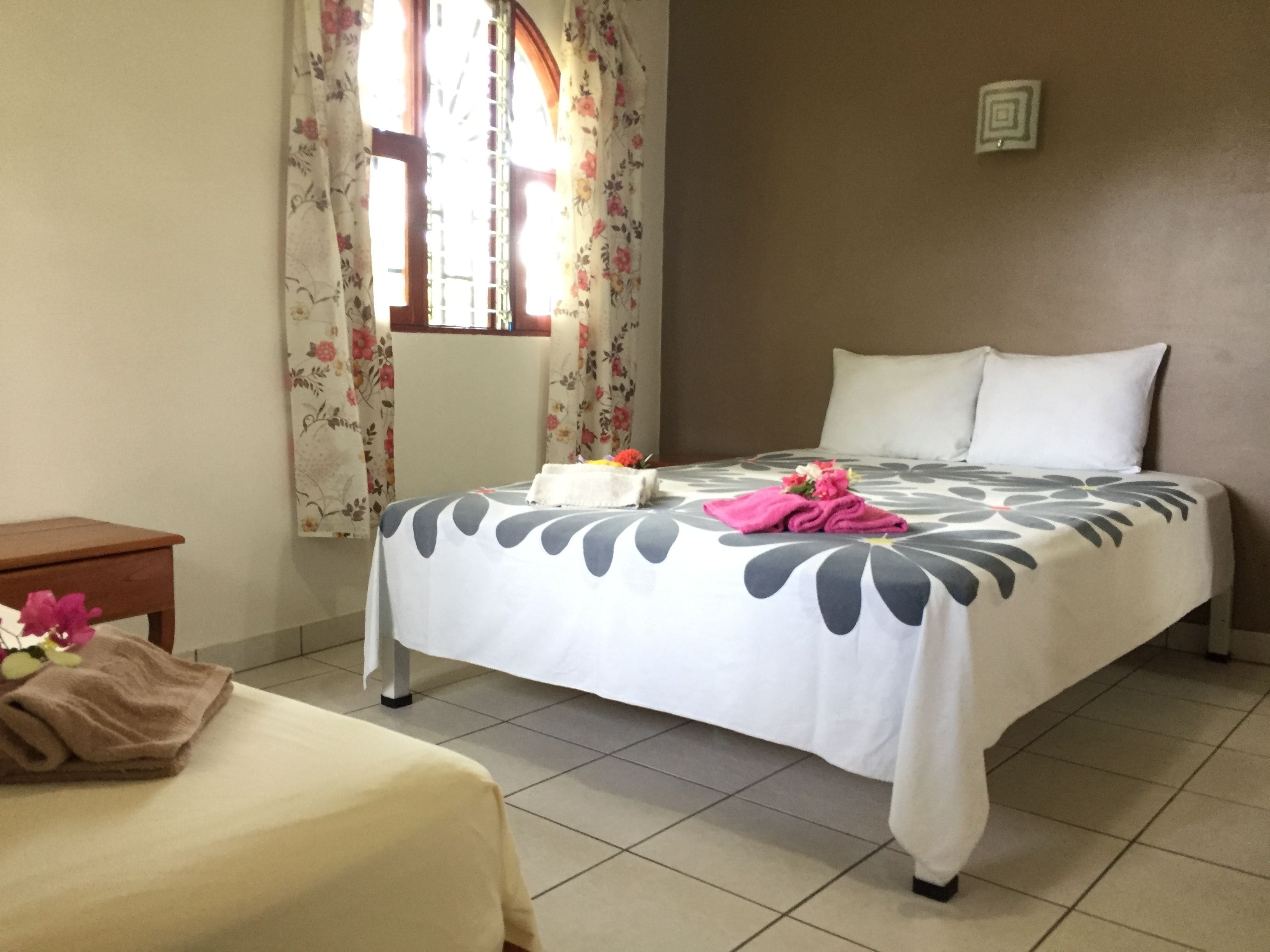 A hotel room with a bed, a small bedside table, and a window with floral curtains.