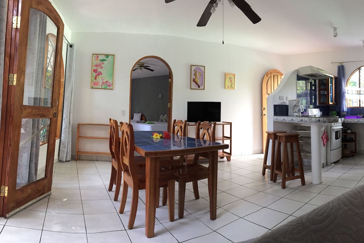 A spacious living room with a dining area, a kitchen with a window, and a ceiling fan.