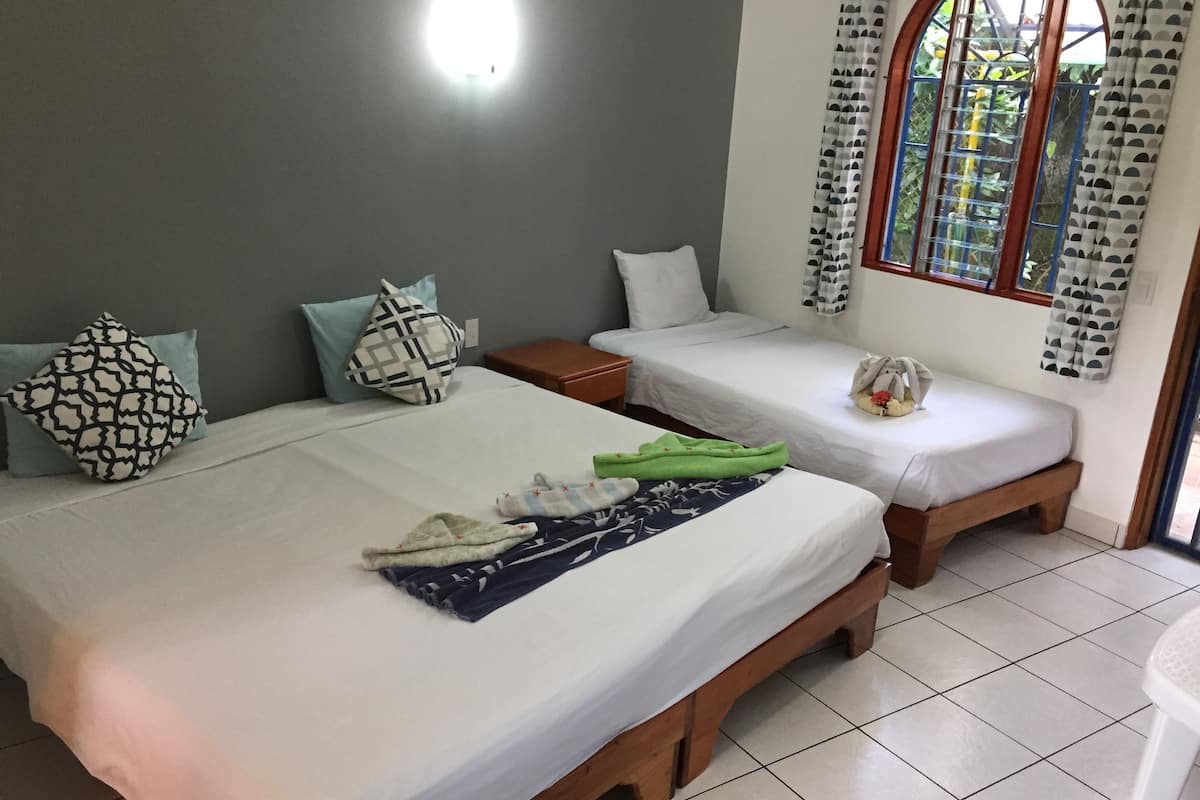 A hotel room with two single beds, a nightstand, a small table, and a window with curtains.