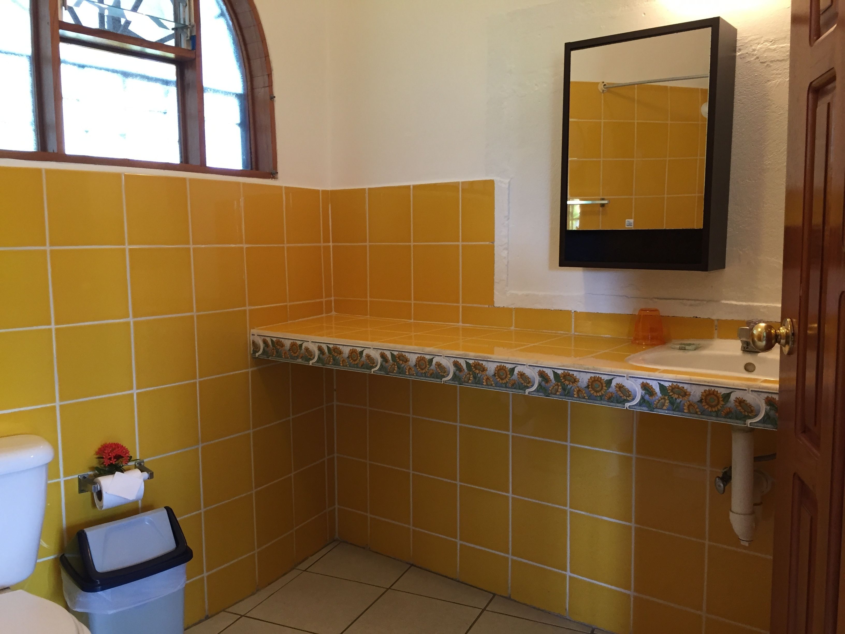 A bathroom with yellow tiles, a white sink, a mirror, and a toilet.