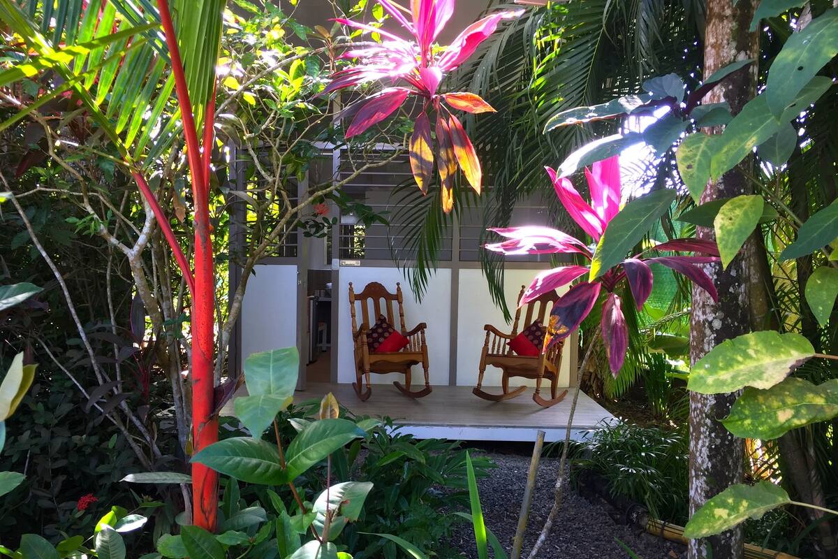 A garden with two rocking chairs and a white building in the background.