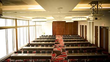 A conference room with rows of tables and chairs, large windows, and a carpeted floor.
