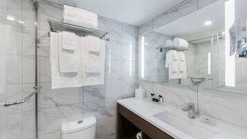 A modern bathroom with a glass shower enclosure, a white toilet, a vanity with a mirror, and a towel rack with white towels.