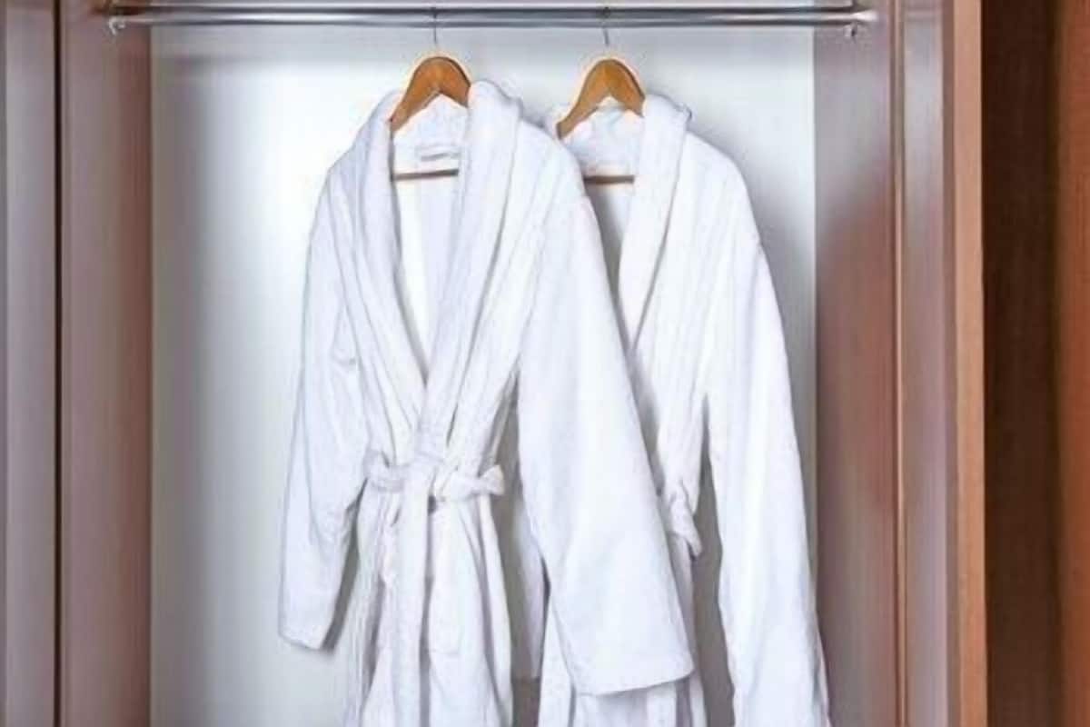 Deux peignoirs blancs sont suspendus à un cintre en bois dans un placard.