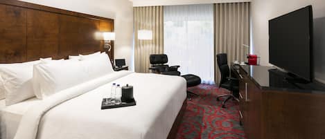 A hotel room with a large bed, a desk with a TV, a chair, and a desk lamp.