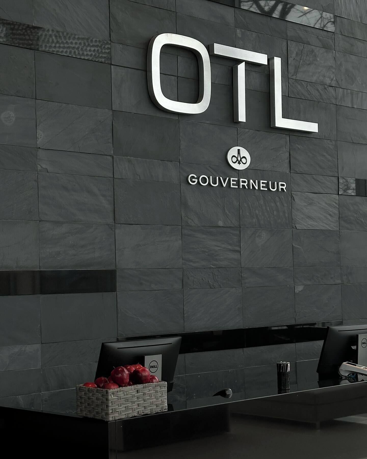 A reception desk with a sign that reads "OTL" and "GOUVERNEUR" on a dark tiled wall.