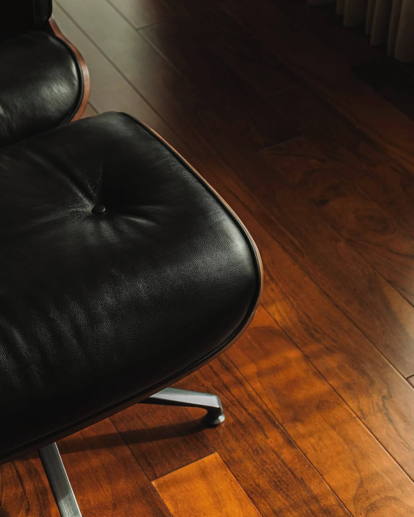 Un fauteuil de bureau en cuir noir, avec des pieds en métal, posé sur un plancher en bois.