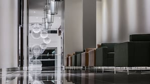 A modern lobby with a reflective floor, a row of seating, and a unique spherical light fixture. - OTL Gouverneur Sherbrooke (Sherbrooke)