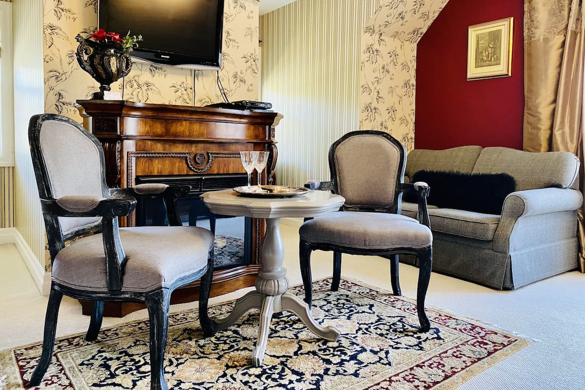 A living room with a piano, two chairs, a sofa, a TV, and a floral wallpaper.