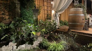 An outdoor garden area with a wooden fence, a stone wall, and various potted plants.