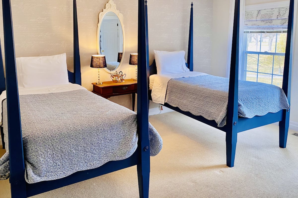A four-poster bed room with a chandelier, a mirror, and a window with a view.
