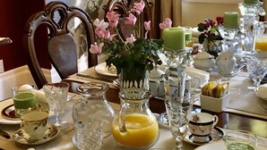 A dining table set for a meal with various glassware, plates, and a vase with flowers.