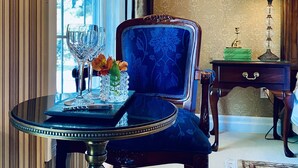 A room with a round table, a blue upholstered chair, a lamp, and a framed picture on the wall.